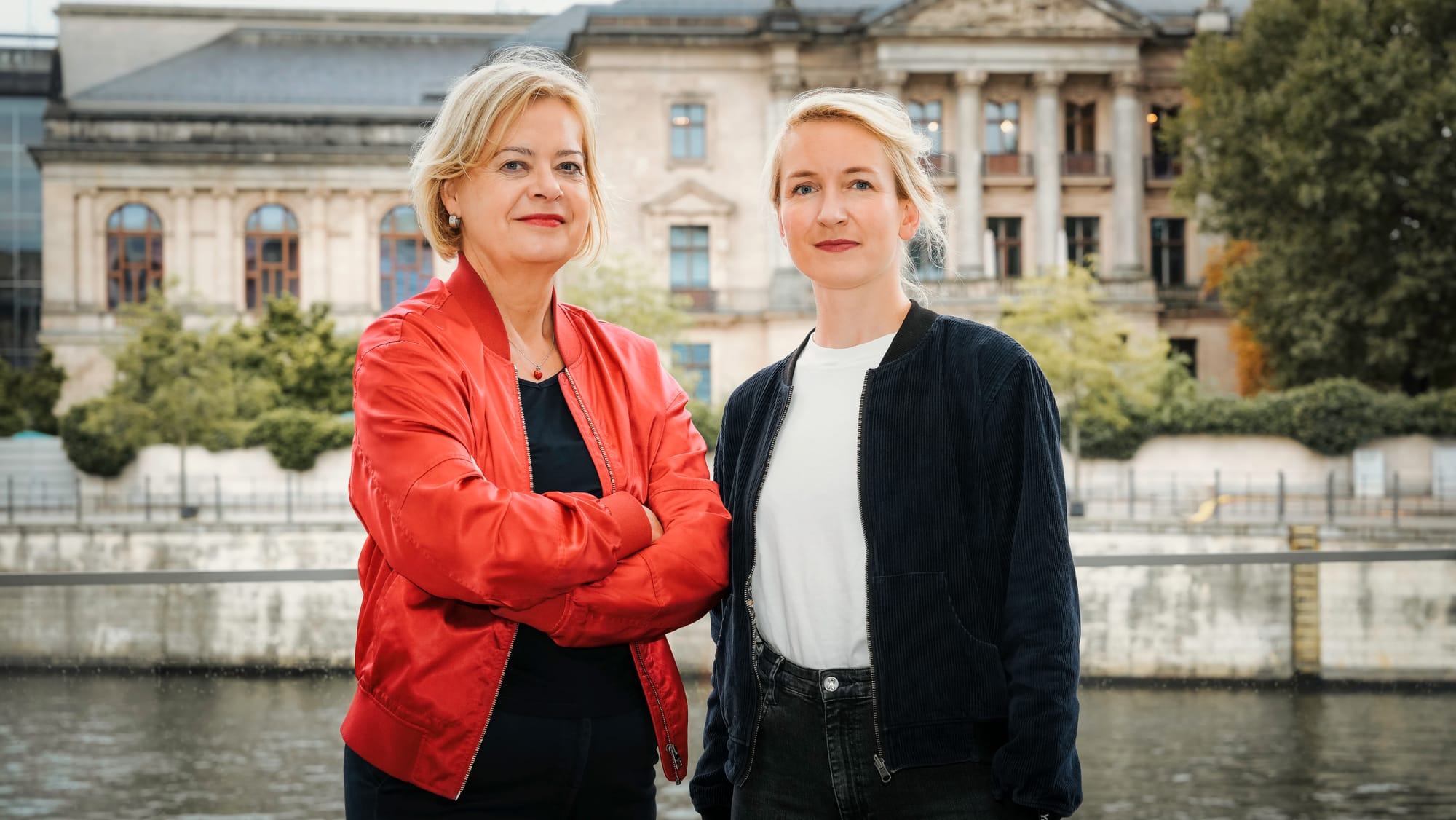 Portrait von Gesine Lötzsch und Ines Schwerdtner. Sie stehen nebeneinander und sehen in die Kamera.