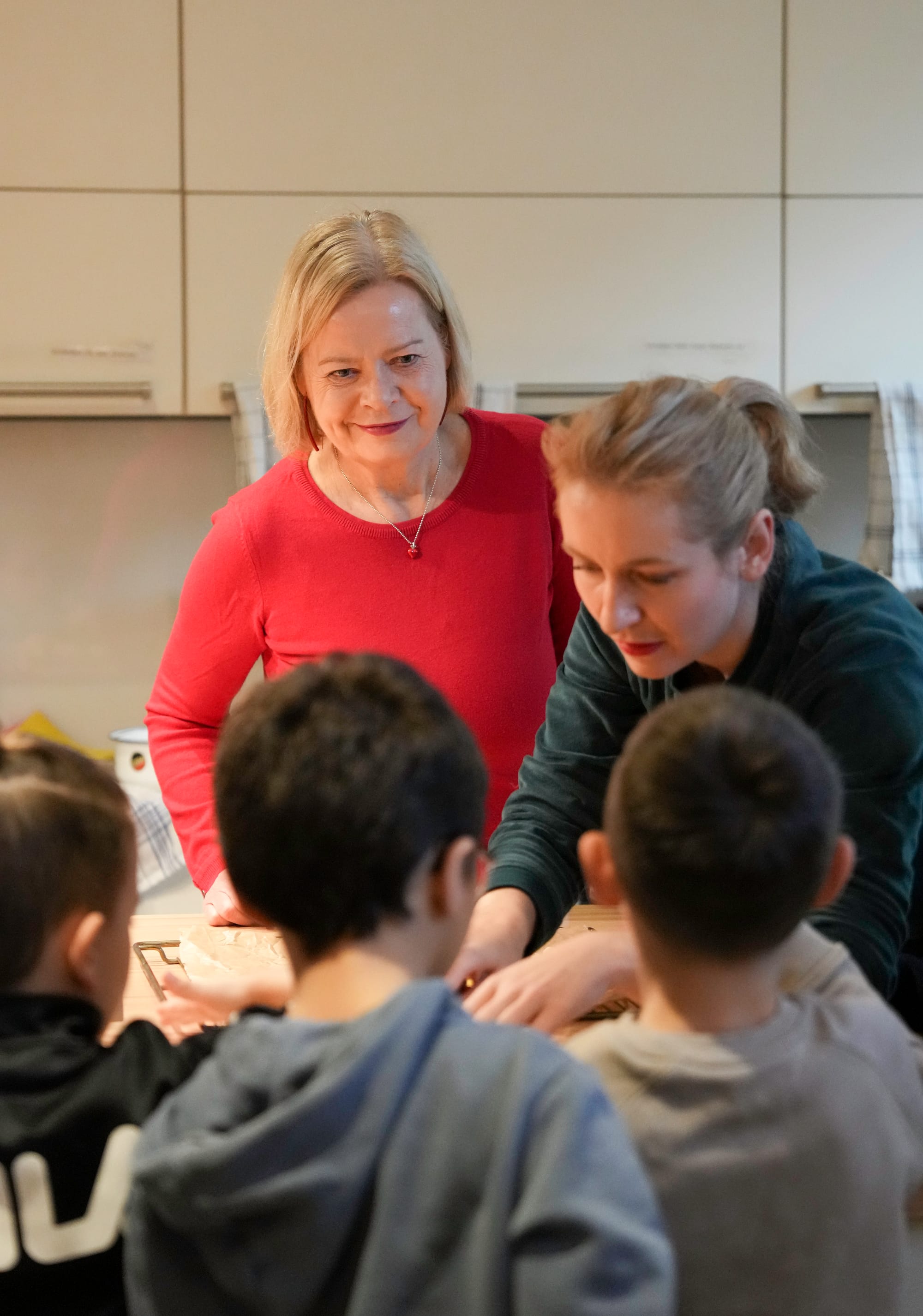 Gesine Lötzsch und Ines Schwerdtner stehen um einen Tisch. Ines beugt sich nach vorne und zeigt den Kindern, die unscharf im Vordergrund zu sehen sind, etwas.