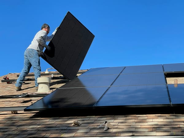 Ein Handwerker steht auf einem Dach und installiert dort ein neues Solarpanel.