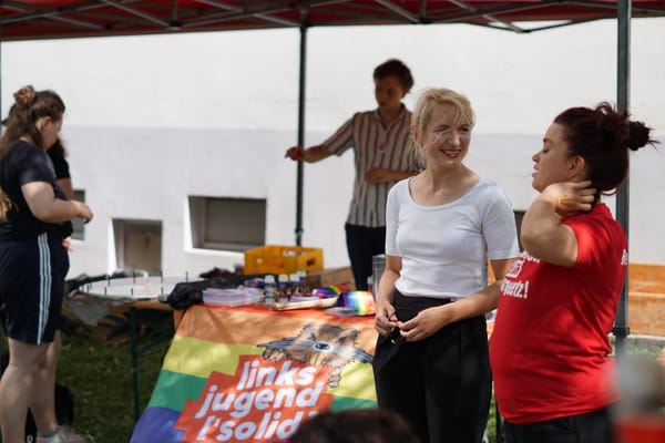 Ines Schwerdtner steht mit einer Genossin in einem roten T-Shirt vor einem Infostand der Linksjugend ['solid] Thüringen.